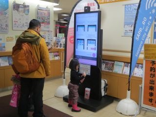 札幌駅観光案内所に設置した47インチのデジタルサイネージとカメラ。デジタルサイネージから札幌市の観光スポットを紹介するカード型パンフ「ささっとパンフ」をダウンロードすることができる