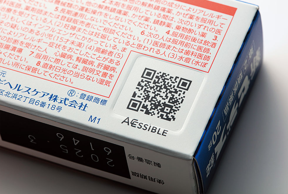 シオノギヘルスケアは医薬品のパッケージに多言語対応のアクセシブルコードを印刷し、「情報」のバリアフリー化を進めている。QRコード部分にはデボス加工を施し、触ると凹（へこ）んでいるのが分かる