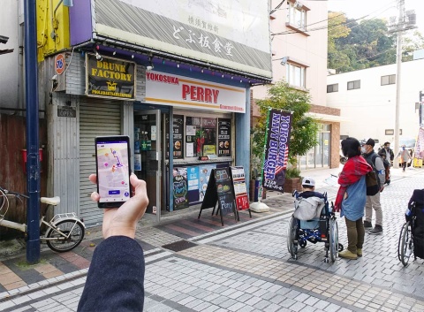 アプリで目的地までのルートを調べながら、横須賀市のドブ板通り商店街を散策する車いす利用者