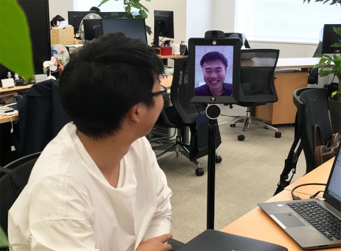 デスクにいる従業員に「最近、仕事はどうですか」と気軽に話しかける楠山氏。笑みがこぼれる。座っている人の目の高さに合わせ、支柱の高さを変えられる
