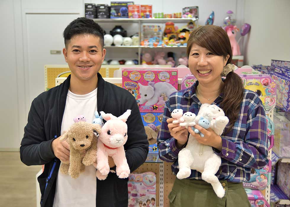 セガトイズ本社のエントランスで商品を抱く土屋氏（左）と伊藤氏。ちなみに「産んじゃったシリーズ」の猫、犬、うさぎのすべての鳴き声と「ハッピーバースデー」の歌は、何人かプロも試したが、結局、開発当時に手伝ってもらった伊藤氏の娘（現在6歳）が本番も担当したという