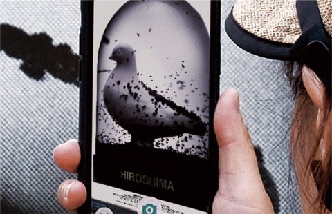 QRコードからダウンロードしたアプリ「aug!」を開いて画像にスマートフォンをかざせば、AR（拡張現実）により、ハトが黒くなる姿などを見られる