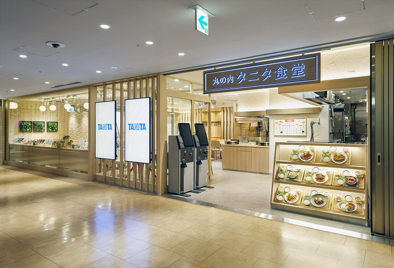 「丸の内タニタ食堂」（東京都千代田区丸の内3-1-1 丸ノ内国際ビルヂング地下1階）。営業時間はランチタイム11～15時、カフェタイム15時～17時半、ディナータイム17時半～22時。席数64。店内もリニューアルし、以前よりリラックス感のある内装に