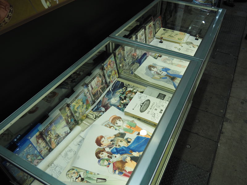 試遊台の右隣には、『アトリエ』シリーズの歴史をまとめたコーナーが。歴代のタイトルを年表にまとめたパネルや、過去作品のパッケージなどが収められたガラスケースが。直筆のキャラクター設定画や、アフレコ台本など、貴重なアイテムが見られるのだ