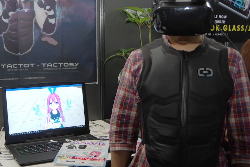 bHapticsブースとIVRのコラボタイトル「つんつんVR」。触感スーツ「TACTSUIT」はかなりサイバーなデザイン。だが、ゲーム内容は美少女や美少年に体のさまざまな部分をつつかれて触感を楽しむというものだ