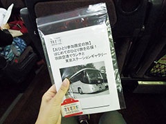 クラブツーリズムの専用バス。乗車する前に配られたのは、しおり、羽田空港と東京駅の構内地図のコピー、ツアー参加者用のバッジ。しおりには、今日のスケジュールのほか、ひとり旅の説明が書かれている。バッジの裏には添乗員の携帯電話番号が手書きされていた